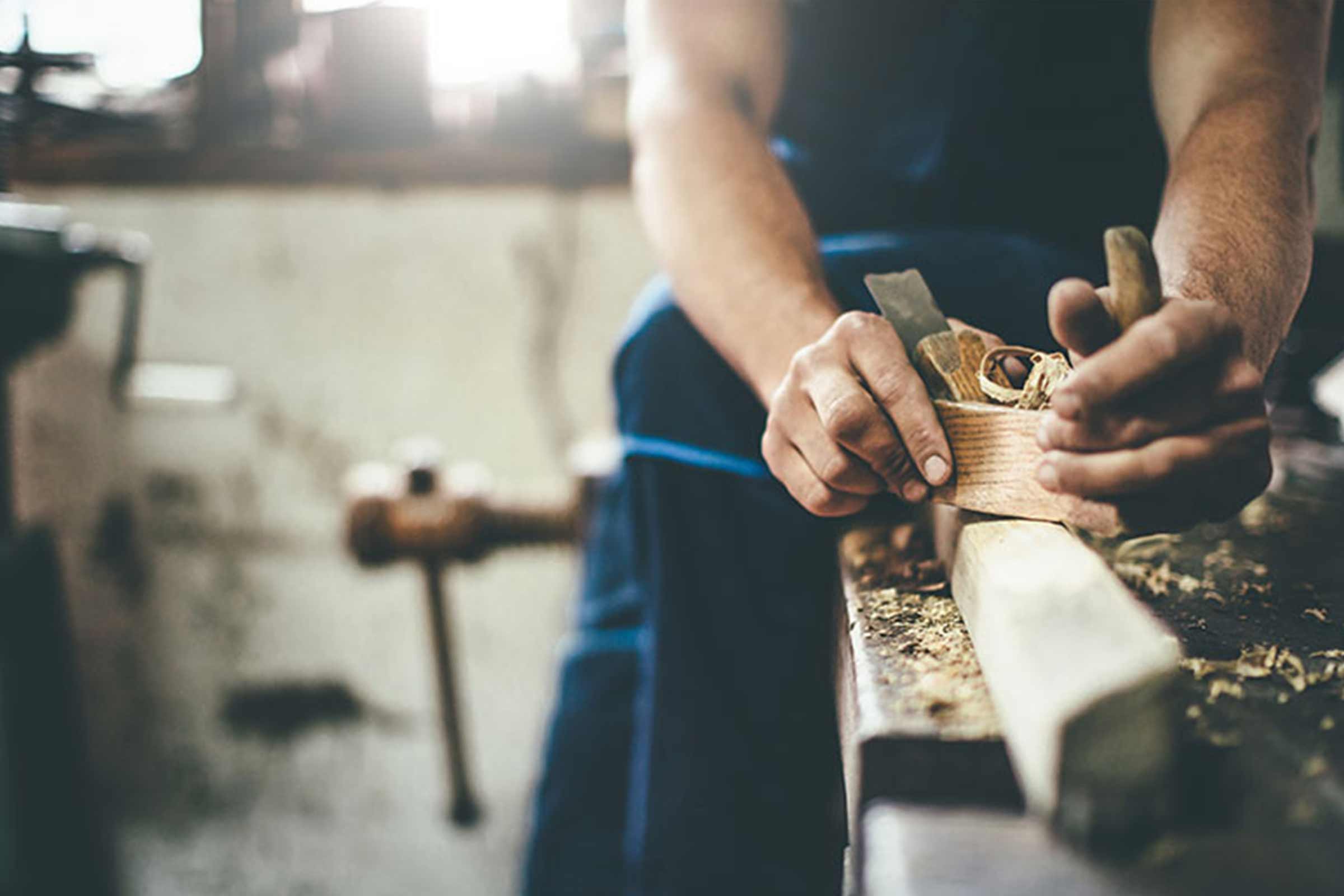 Ein Mann hobelt ein Stück Holz mit einem Hobel.