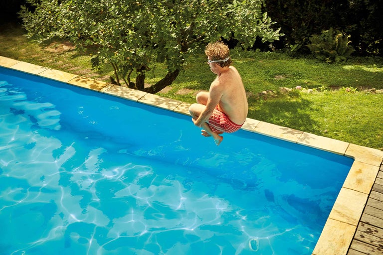 Mann springt in privates Schwimmbecken im Garten