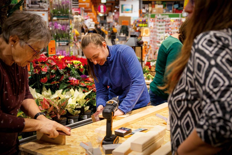 Personen arbeiten mit Holz und Werkzeugen an einem Tisch im Hornbach Markt.