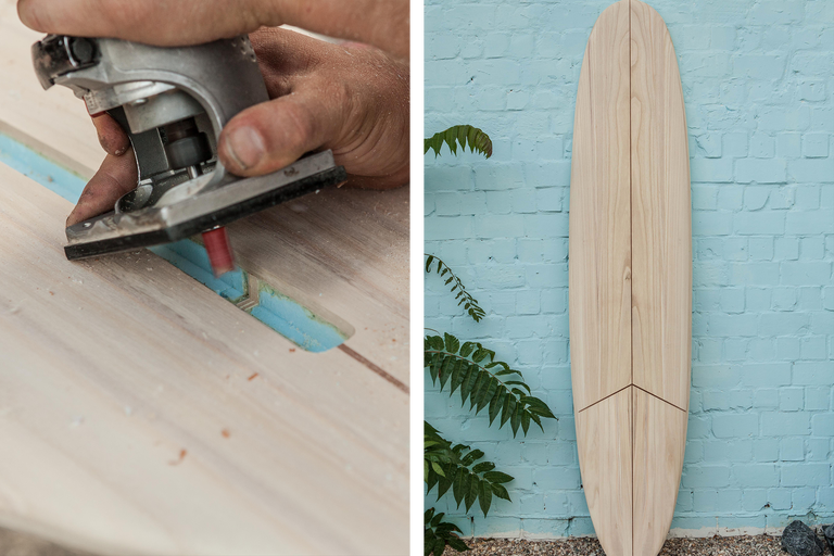 Person bearbeitet ein Holzbrett mit einer Oberfräse; daneben steht ein hölzernes Surfbrett an einer Wand