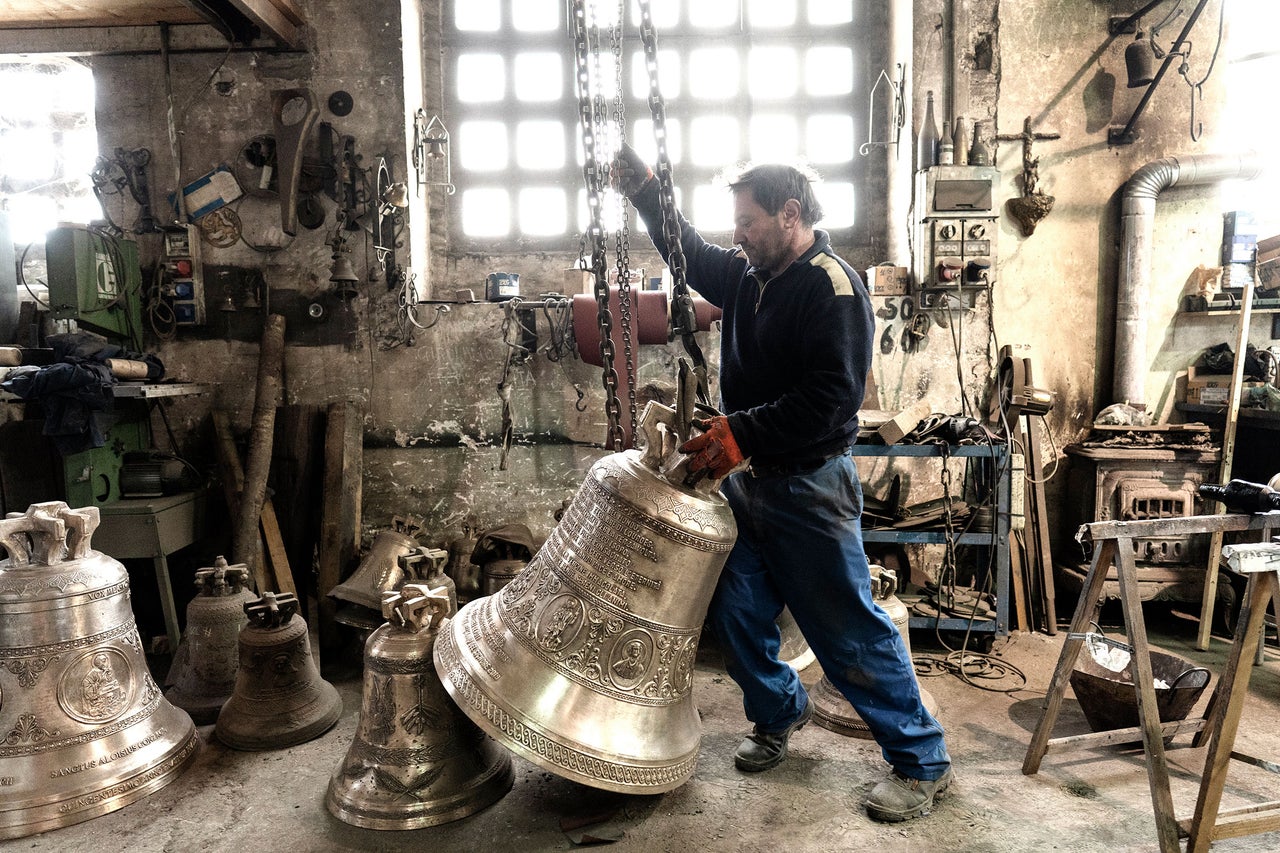 Ein Handwerker in einer Werkstatt hantiert mit einer großen Glocke an einer Kette.
