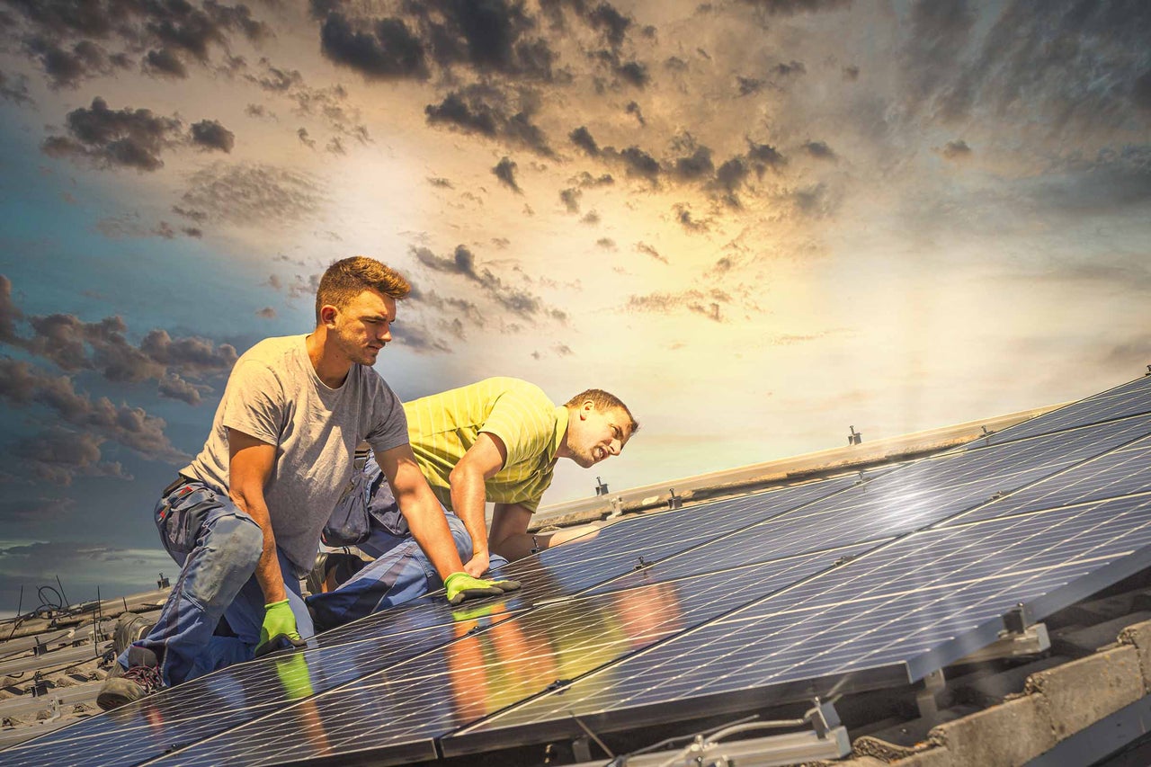 Zwei Monteure installieren Solarmodule auf einem Dach, umweltfreundliche Energielösung.
