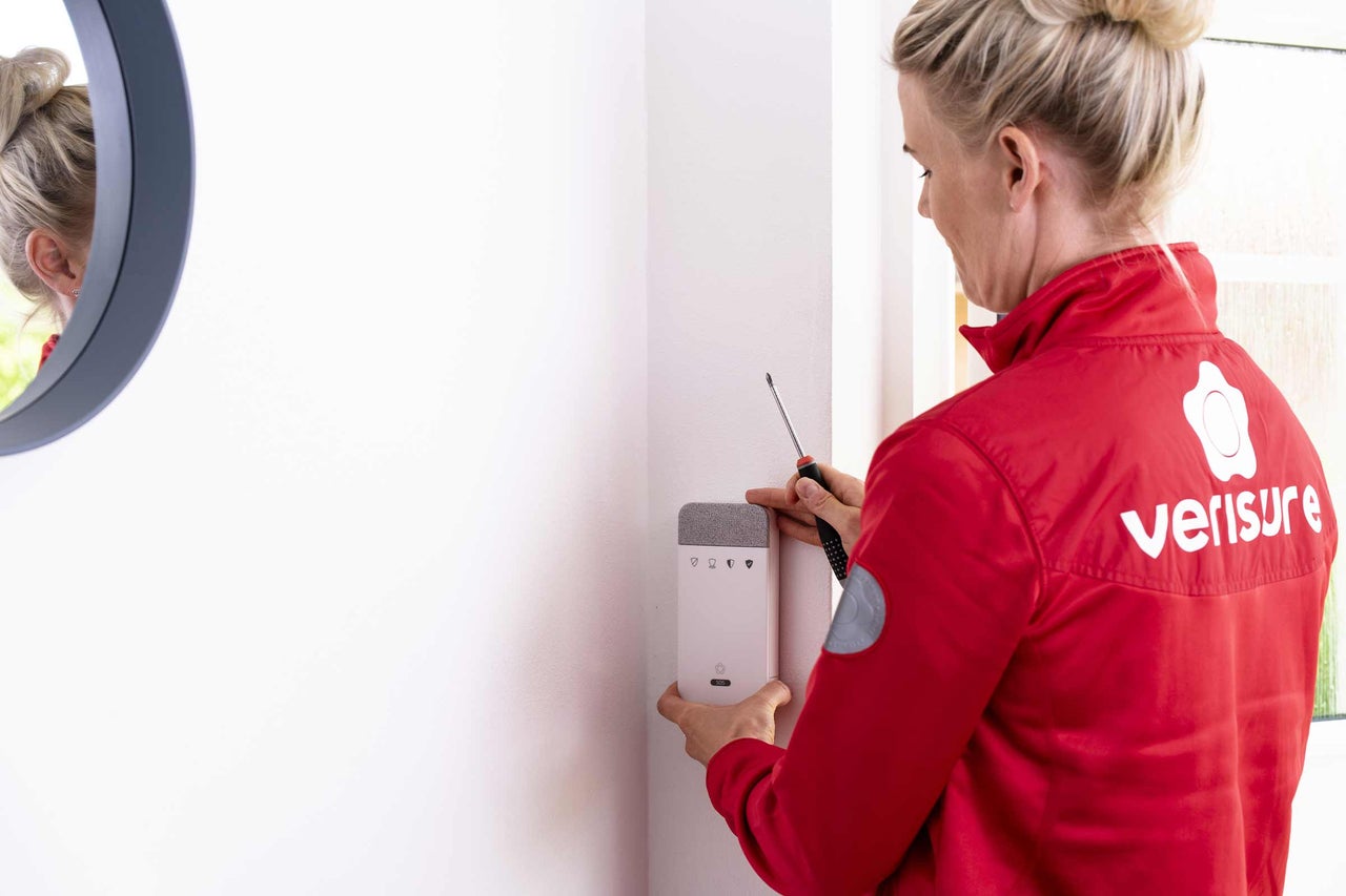 Eine Frau installiert ein Verisure-Sicherheitssystem mit einem Schraubenzieher an einer Wand.