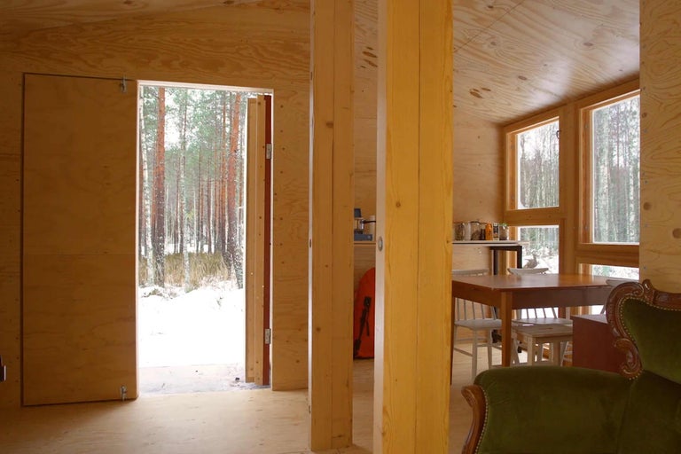 Innenraum eines Holzhauses mit Blick auf einen winterlichen Wald.