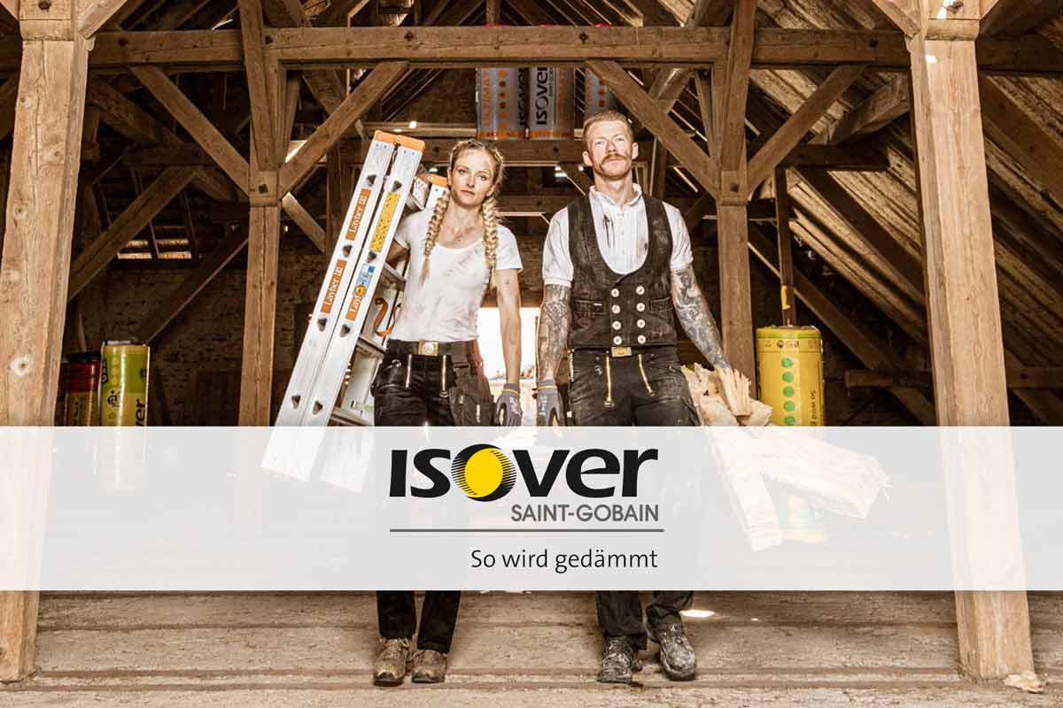 Zwei Handwerker in Arbeitskleidung in einem Dachgeschoss mit einer Leiter und Dämmmaterial. Isover Logo.