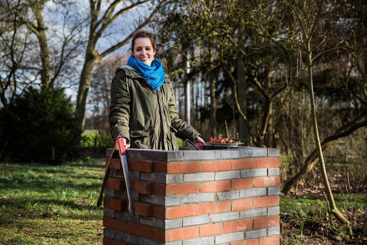 Frau grillt auf einem gemauerten Grill im Garten