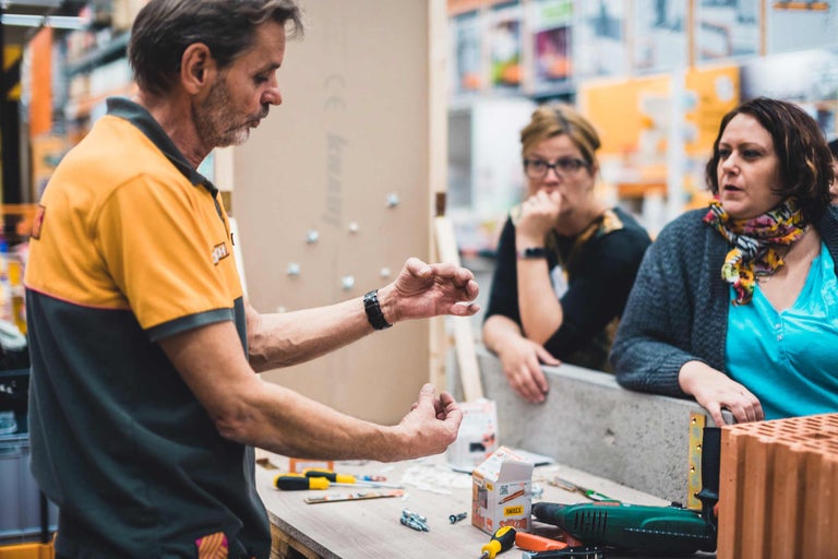 Ein Handwerker erklärt zwei Kundinnen verschiedene Werkzeuge und Baumaterialien im Hornbach Baumarkt.