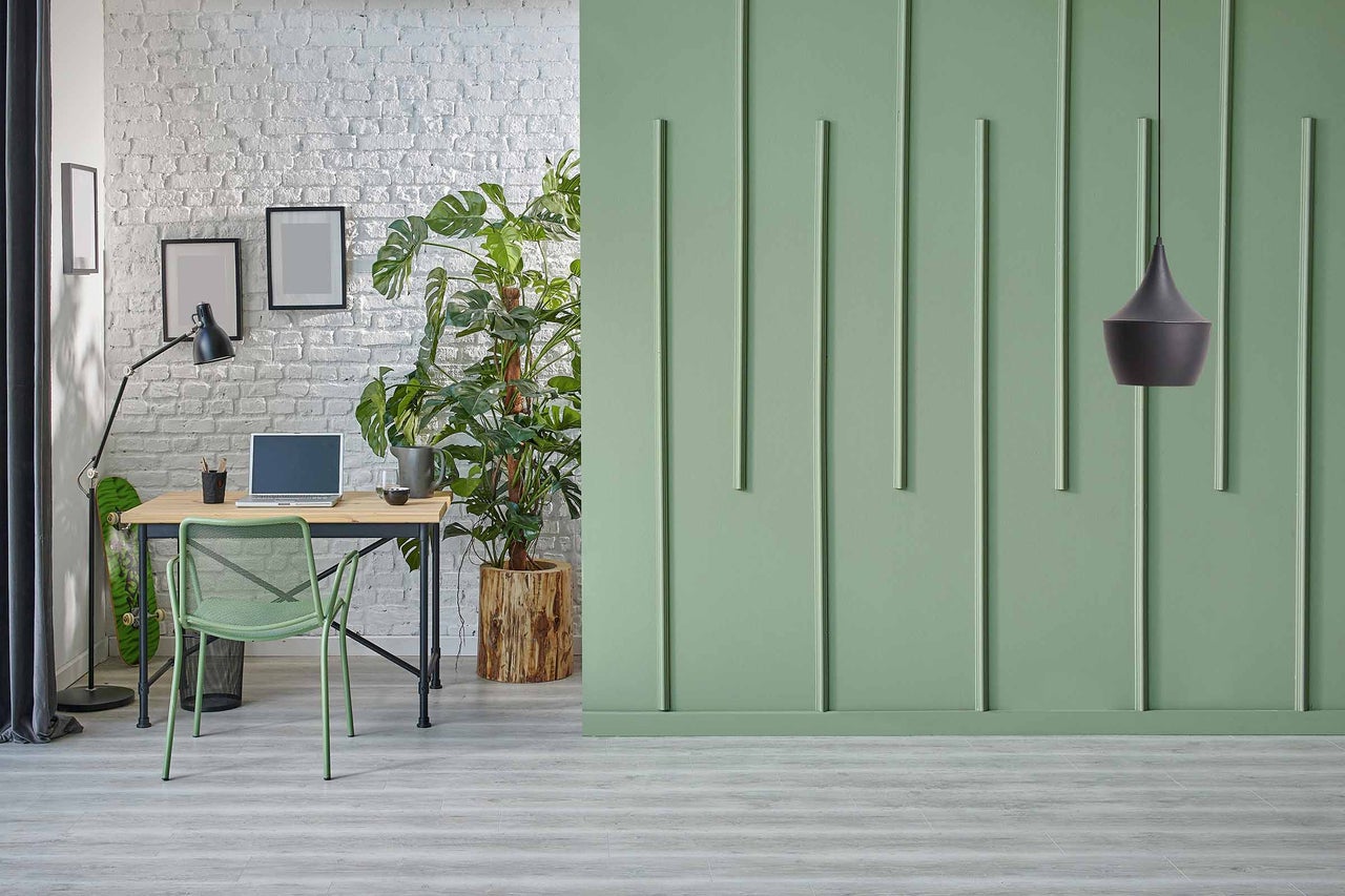 Helles Arbeitszimmer mit Schreibtisch, Stuhl und Zimmerpflanze vor einer grünen Wand