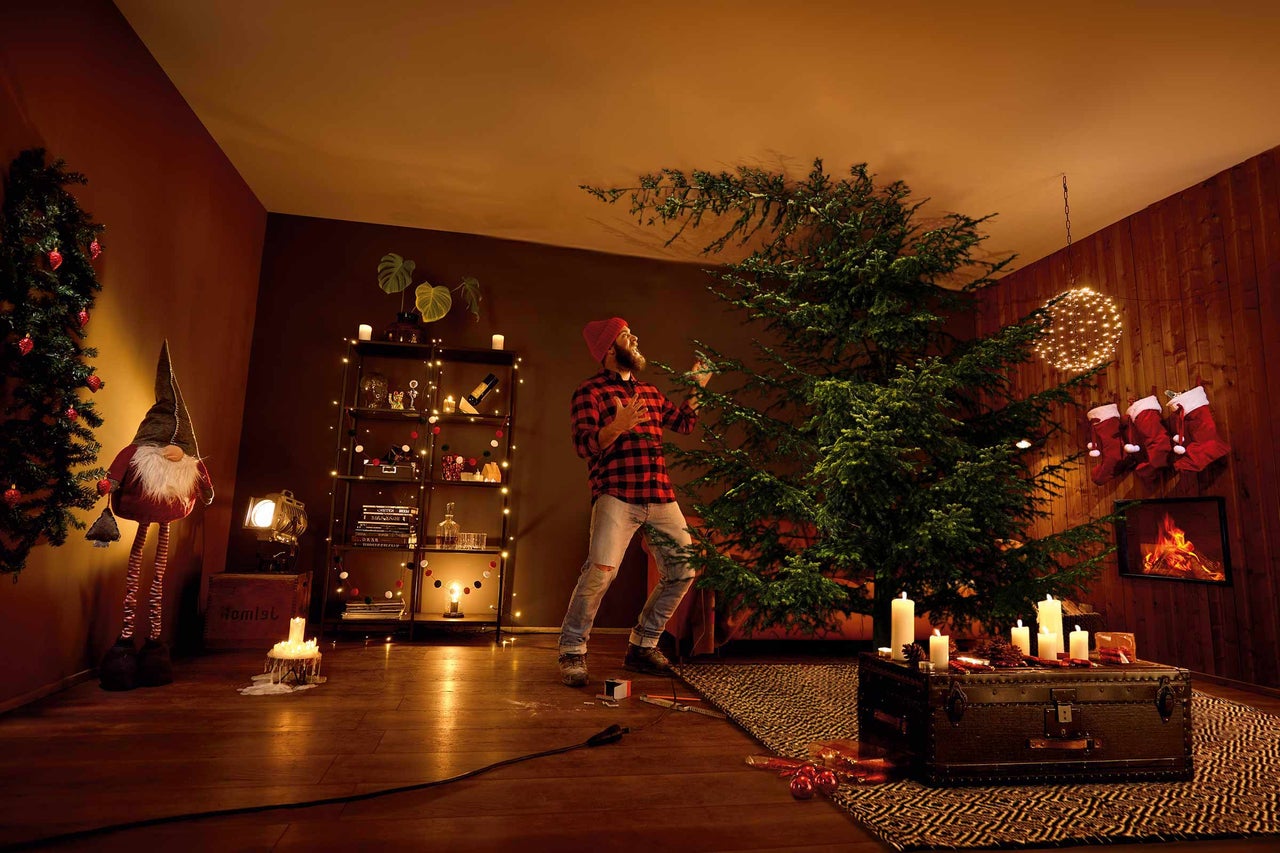 Wohnzimmer mit geschmücktem Weihnachtsbaum und Mann, der Weihnachtsbaumschmuck anbringt