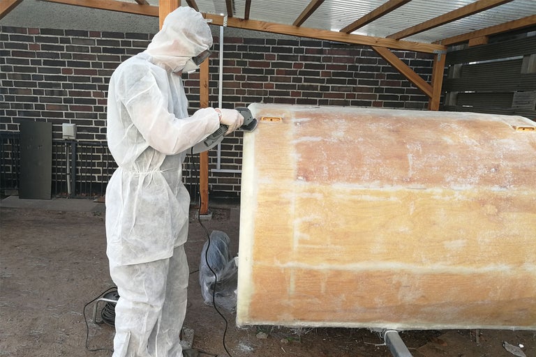 Person mit Schutzanzug schleift eine Oberfläche mit einem Schleifwerkzeug.