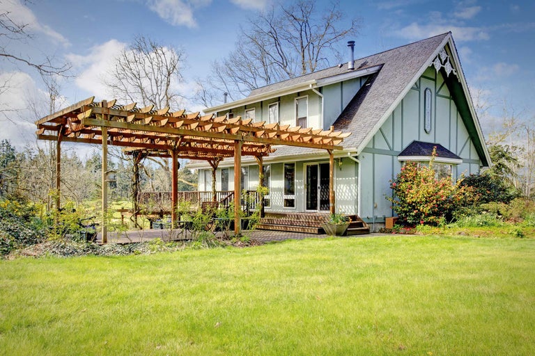 Ein Haus mit einer Holzpergola, einer Terrasse und einem Rasen.