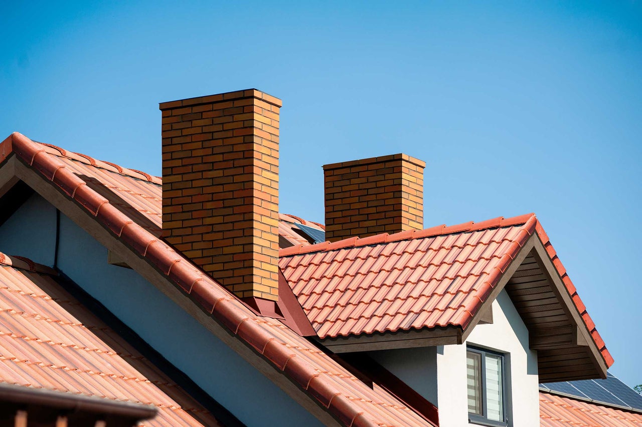 Dach mit Ziegeln und gemauerten Schornsteinen vor blauem Himmel