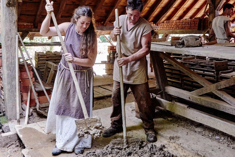 Zwei Personen mischen mit Schaufeln Mörtel auf einer Baustelle.