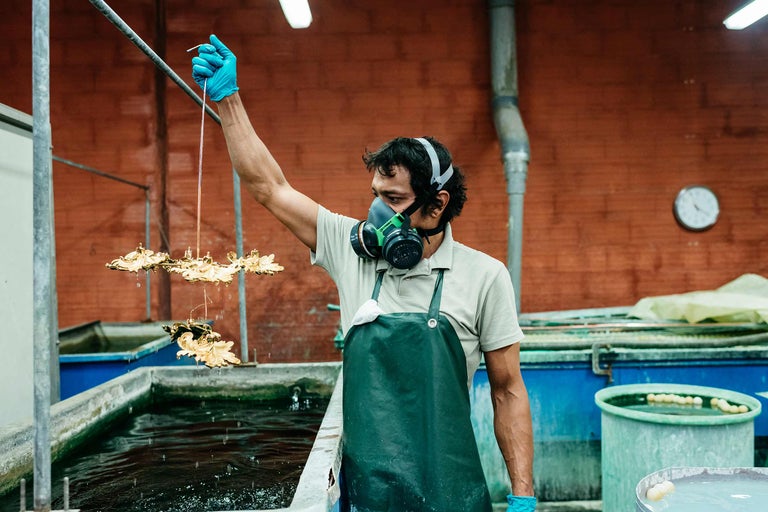Ein Arbeiter mit Schutzmaske und Handschuhen taucht goldene Ornamente in ein Wasserbecken
