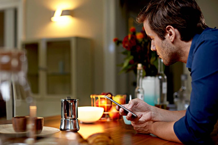 Mann blickt auf ein Smartphone auf einem Küchentisch mit Kaffeekanne