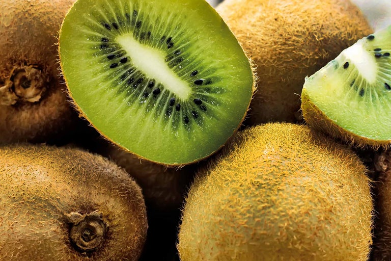 Mehrere Kiwis, eine halbiert, mit Fruchtfleisch und Kernen