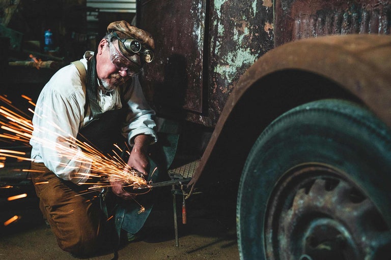 Mann mit Schutzbrille arbeitet mit einem Winkelschleifer an einem Oldtimer