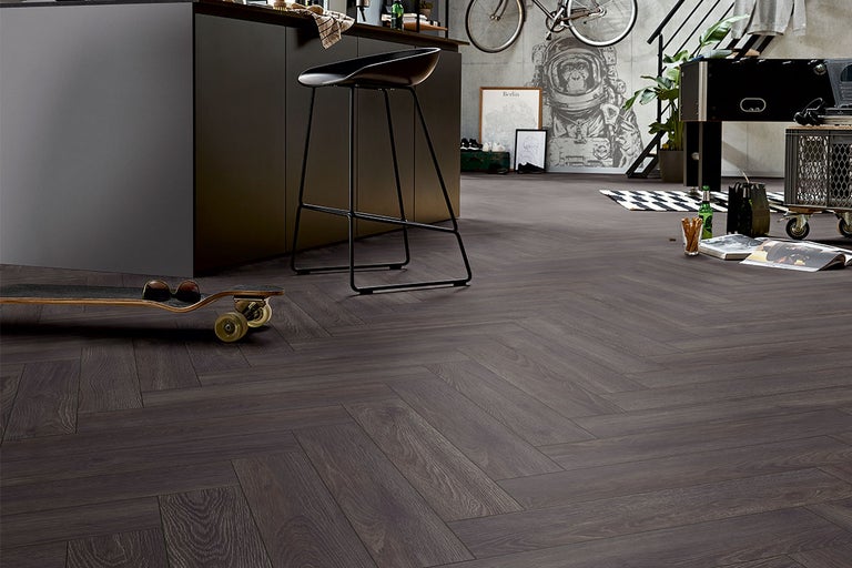 Innenraum mit dunklem Holzboden im Fischgrätmuster, ergänzt durch eine Kücheninsel, einen Barhocker und dekorative Elemente