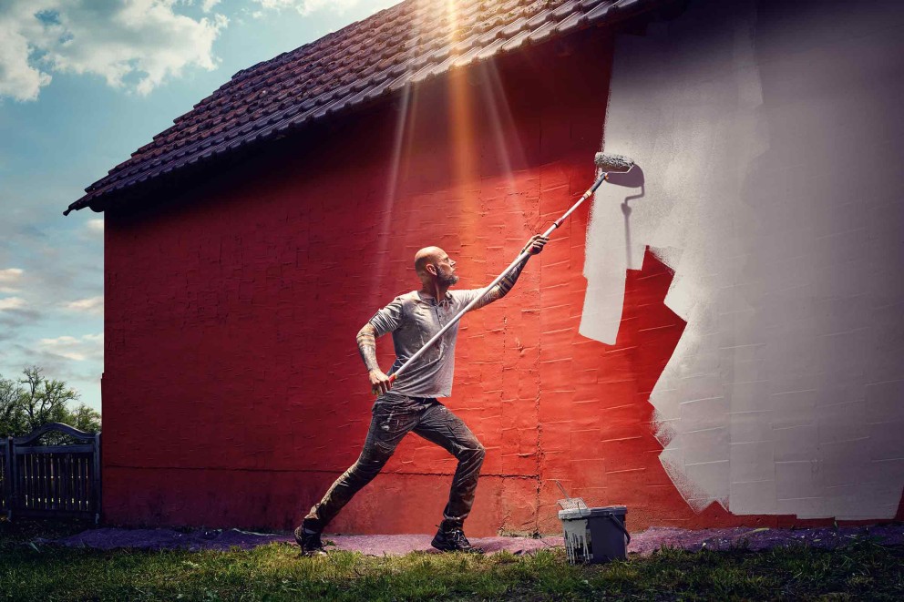 Ein Mann streicht eine Hauswand mit einer Farbwalze und Farbe.