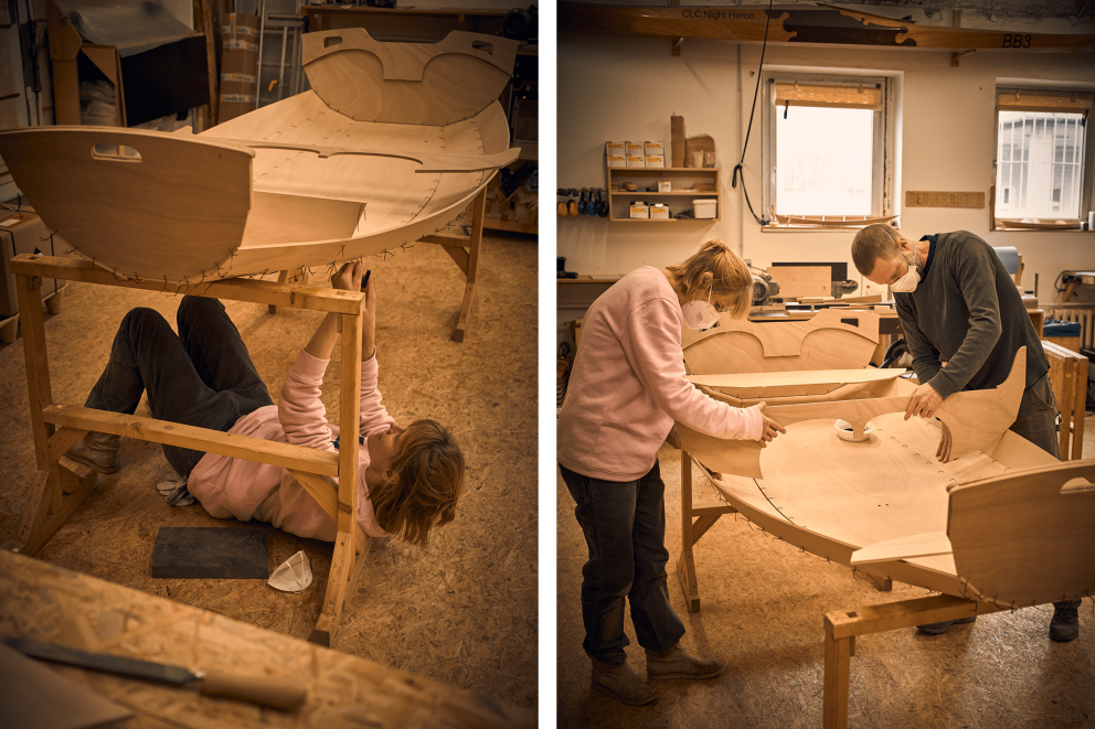 Zwei Personen bauen ein Holzboot in einer Werkstatt.