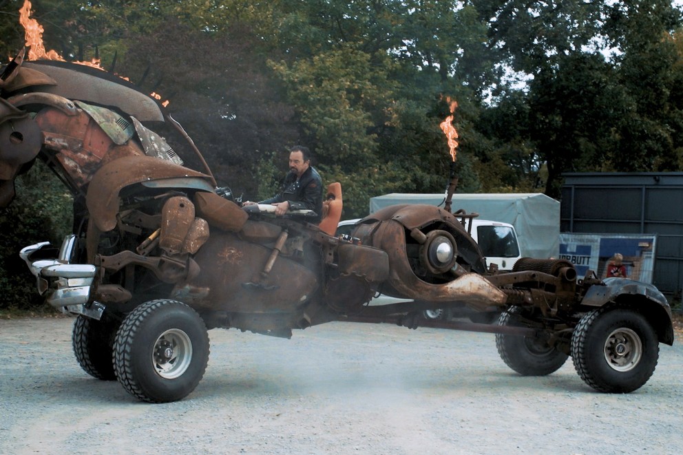 Mann fährt ein Fahrzeug aus Metallschrott mit Flammen.