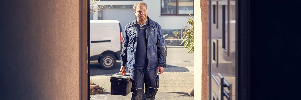 Handwerker mit Werkzeugkoffer vor einem Haus