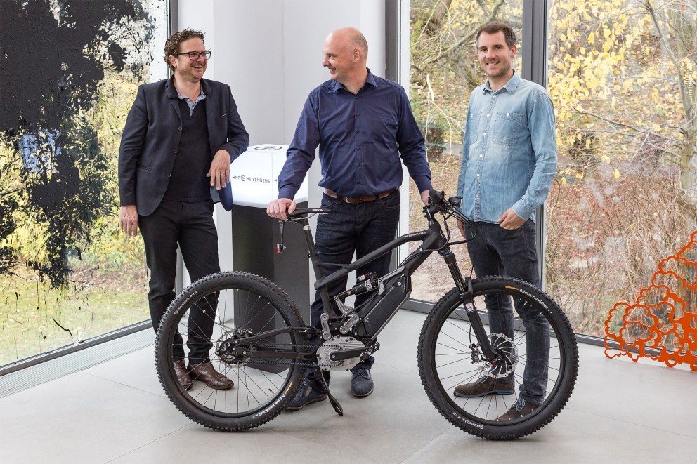 Drei Personen präsentieren ein HNF Heisenberg E-Bike in einem hellen Raum.