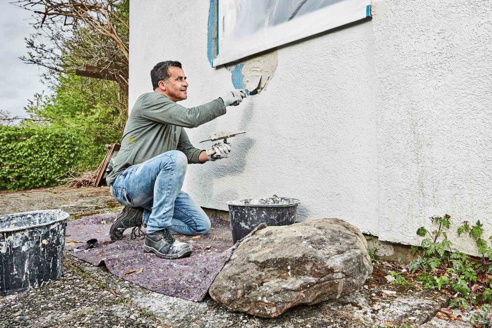Handwerker bei der Fassadenrenovierung mit Spachtel und Putz.