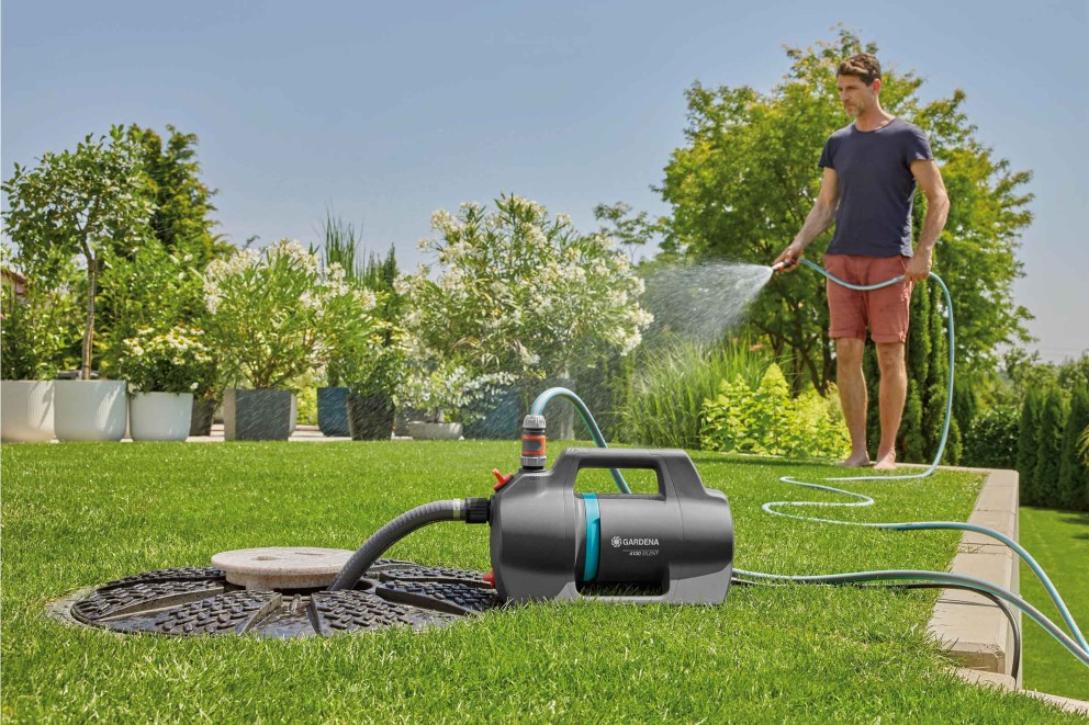 Gartenszene mit Mann, der mit einer Gartenpumpe von Gardena Pflanzen bewässert