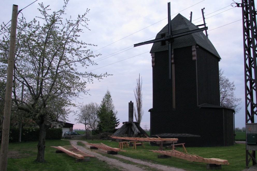 
				Am Weg zum Grundstück der Wernickes liegen vor der fertig verkleideten Mühle die Flügel auf Holzblöcken.

			