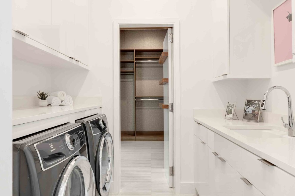 Heller Waschraum mit Waschmaschine, Trockner, Ablagefläche, Waschbecken und begehbarem Kleiderschrank