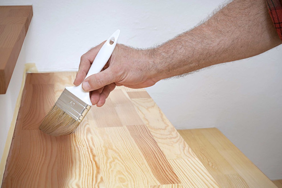 Ein Handwerker lackiert eine Holztreppe mit einem Pinsel.