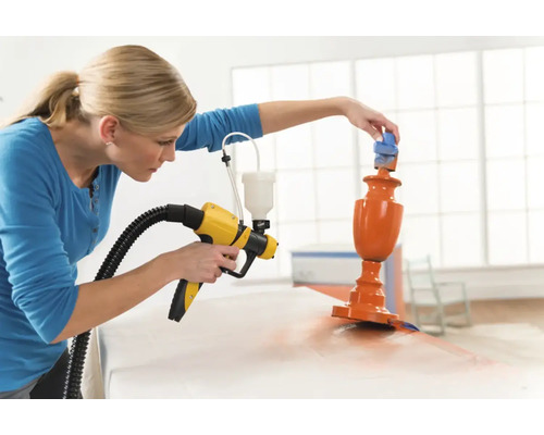 Frau benutzt Farbsprühgerät zum Lackieren eines Objekts.