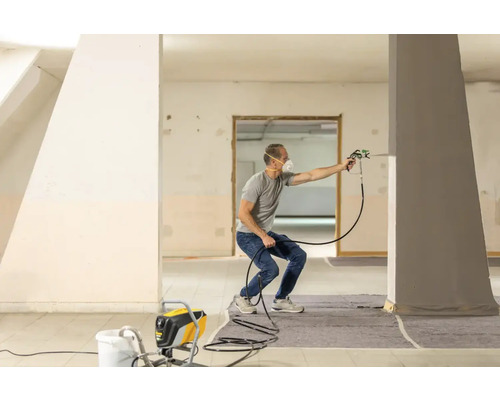 Mann verwendet ein Farbspritzgerät in einem Raum, um eine Säule zu streichen
