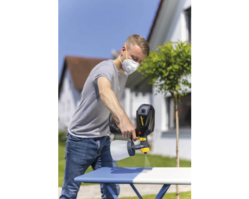 Ein Mann verwendet ein Farbsprühgerät zum Lackieren eines Tisches im Freien.