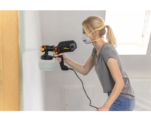 Eine Frau sprüht Farbe mit einem Farbsprühgerät auf eine Wand.