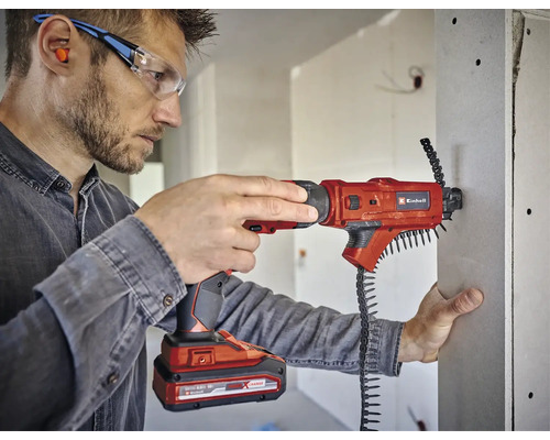 Ein Mann verwendet einen Akku-Trockenbauschrauber von Einhell, um eine Gipskartonplatte zu befestigen. Er trägt dabei eine Schutzbrille und Ohrstöpsel.