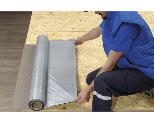 Eine Person rollt eine Baufolie auf einer Holzoberfläche aus.