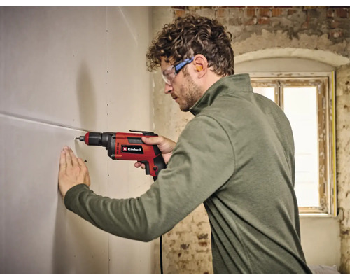 Mann bohrt mit einer Einhell Bohrmaschine ein Loch in eine Wand.