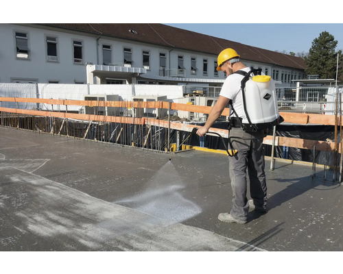 Mann verwendet eine Rückenspritze auf einer Baustelle, um Beton zu behandeln.