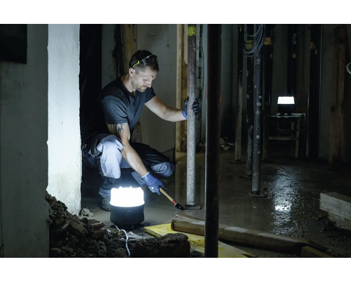 Bauarbeiter arbeitet im Keller mit einer Akku-Baustellenleuchte für Beleuchtung