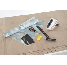 Tapete mit geometrischem Muster, Kleisterbürste, Nahtroller, Tapetenmesser, Andrückspachtel und Schere auf einem Tisch.