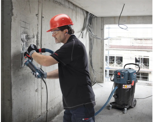 Handwerker mit Mauernutfräse und Staubsauger beim Arbeiten an einer Betonwand auf einer Baustelle