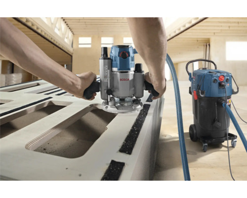 Person fräst Holz mit einer Oberfräse der Marke Bosch und einem Staubsauger