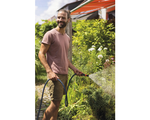 Ein Mann bewässert mit einem Gartenschlauch Pflanzen im Garten.