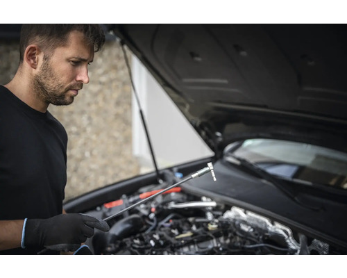 Mann mit Steckschlüssel und geöffneter Motorhaube eines Autos