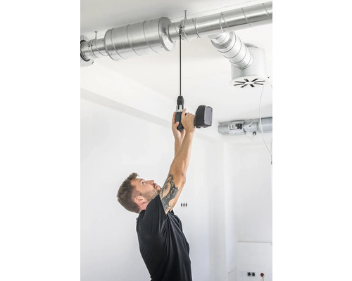 Mann montiert Lüftungsrohr mit Akkubohrer an der Decke.
