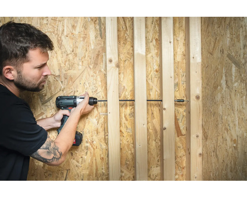 Mann schraubt mit einem Akkubohrschrauber Holzlatten an eine Holzspanplatte