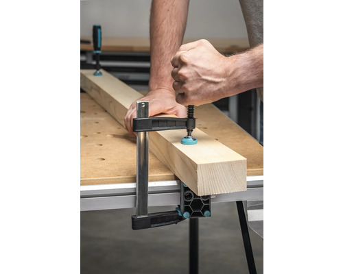 Person befestigt Holzstück mit einer Schraubzwinge auf einer Werkbank.