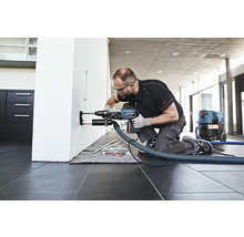 Ein Mann bohrt mit einer Schlagbohrmaschine und Staubabsaugung ein Loch in eine Wand.